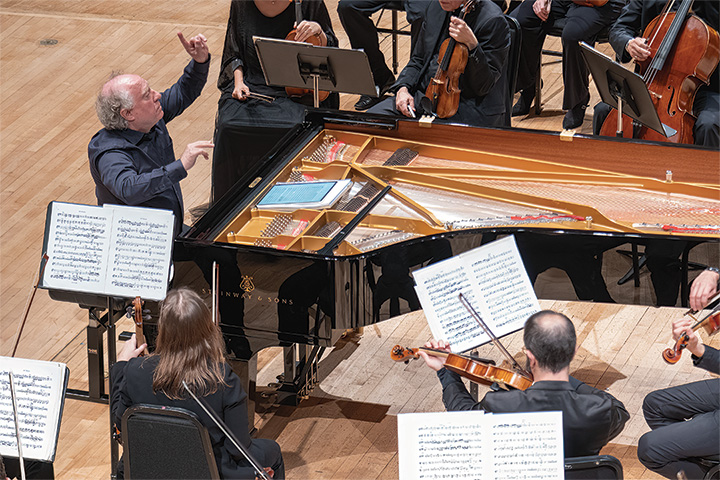Jeffre Kahane conducts the members of the Harmonium of Texas while standing behind a Steinway grand piano
